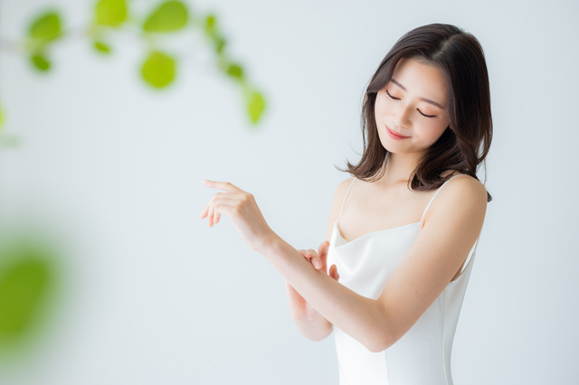 白いキャミソールを着て腕の肌に触れている女性