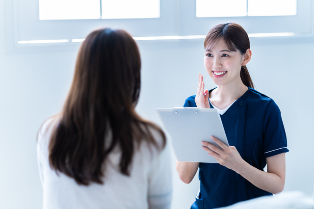クリニックの女性スタッフがクリップボードを持って女性に説明している様子