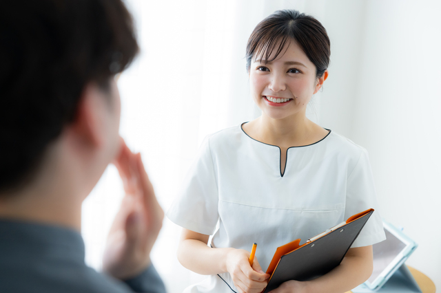 白衣のスタッフがクリップボードを持って男性に説明しているカウンセリングの場面