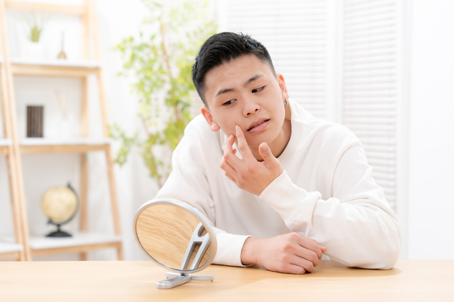 手鏡を見ながら頬のヒゲの状態を確認している男性