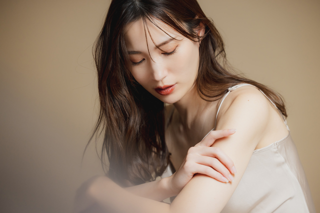 ベージュの背景で二の腕の肌にそっと触れている女性